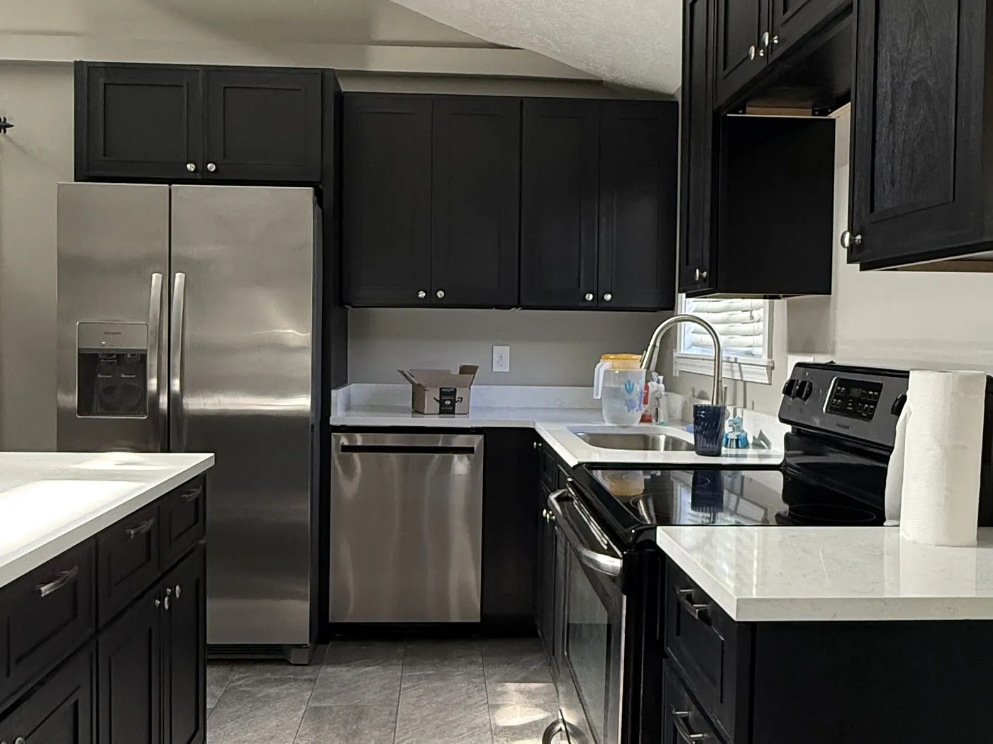 The finished galley run with quartz counters, dark cabinetry, stainless range and dishwasher, and tile flooring.