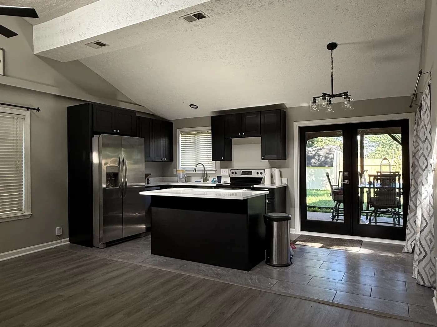The finished kitchen seen from the living area, with dark cabinetry, a quartz-topped island, stainless appliances and new flooring running through both rooms.