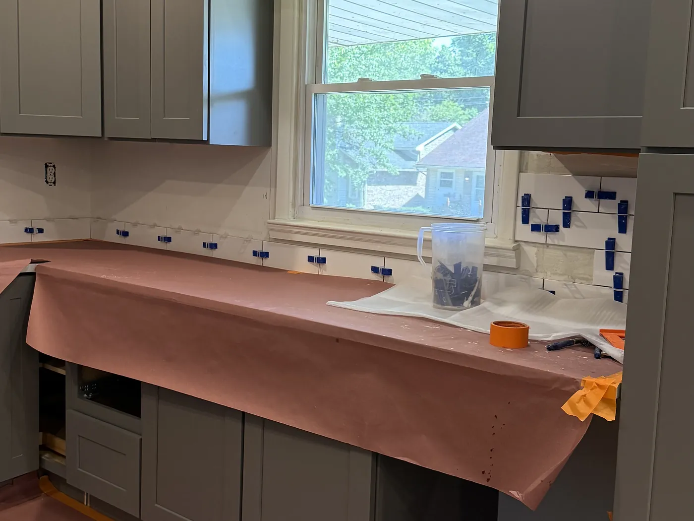 Subway tile backsplash being installed with leveling clips over counters masked with protective paper.