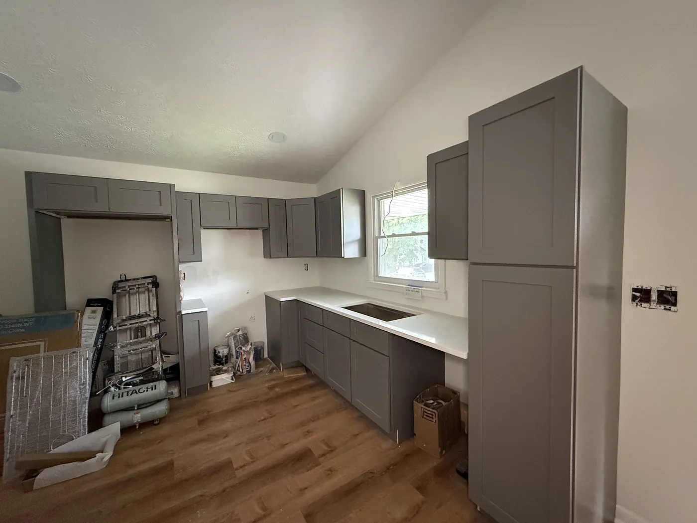 Kitchen mid-build with gray shaker cabinets and quartz counters installed against bare drywall, before the backsplash and fixtures went in.