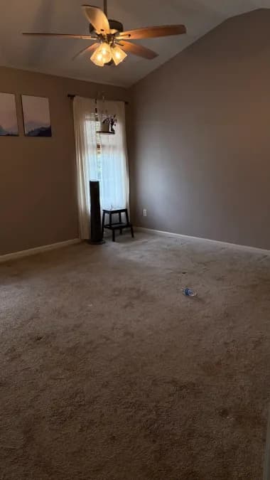 Carpeted room with a ceiling fan and curtained window before repairs at the Georgetown home.