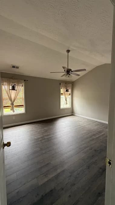 The room after repairs, with plank flooring, gray walls, white trim, and a ceiling fan.