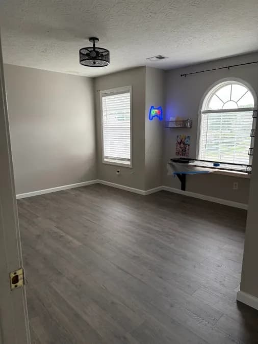 The same room with plank flooring, painted walls, white trim, and an arched window.