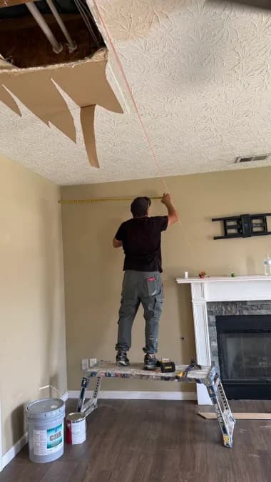 Worker measuring beside the fireplace while part of the ceiling is open.
